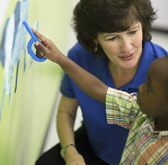 Using the Grabber to Assist Pointing / Joint Attention A boy points to a picture on the wall using the ARK Grabber to guide his hand while a therapist observes