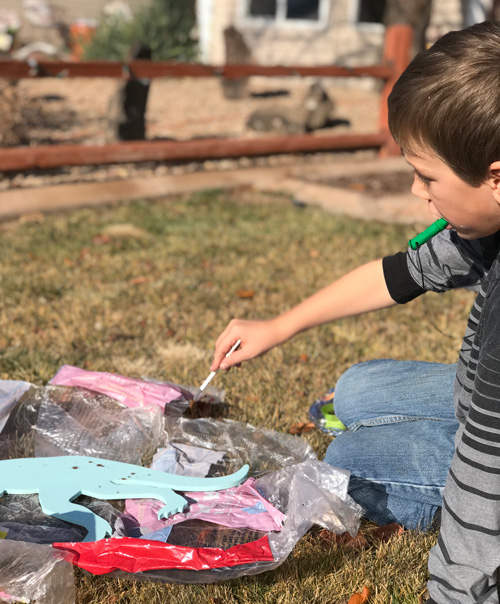 A boy paints outside while chewing on the Bite Saber chewable necklace