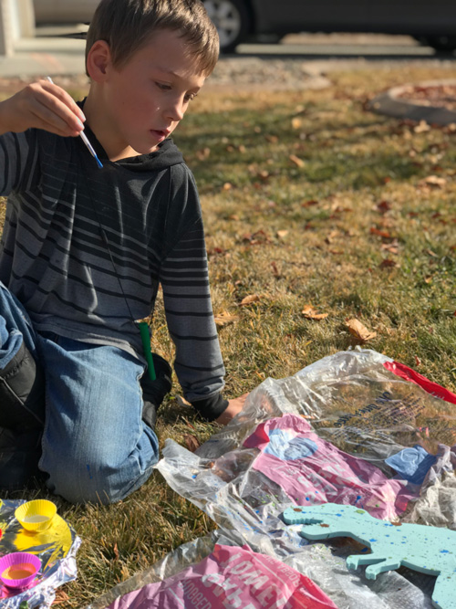 A boy paints outside while wearing the forest green extra extra tough Bite Saber chewelry necklace
