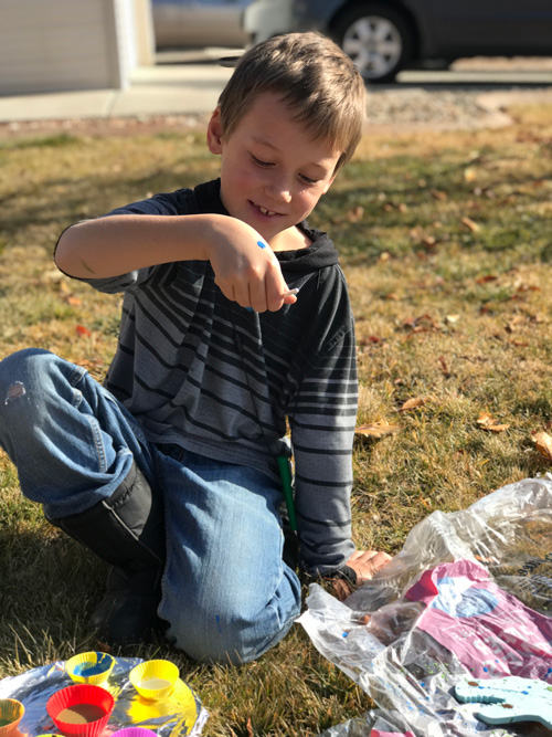 A boy does a fun painting activity outside while wearing an ARK Bite Saber chew necklace