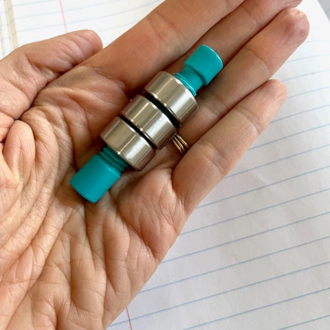 A hand holding the weighted pencil topper (just topper without a pencil) with three weights on it
