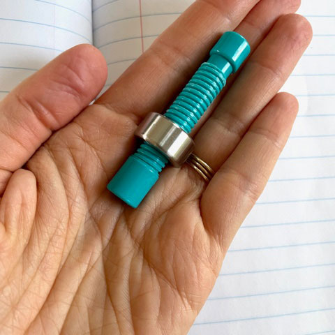 A hand holding the weighted pencil topper (just topper without a pencil) with one weight on it