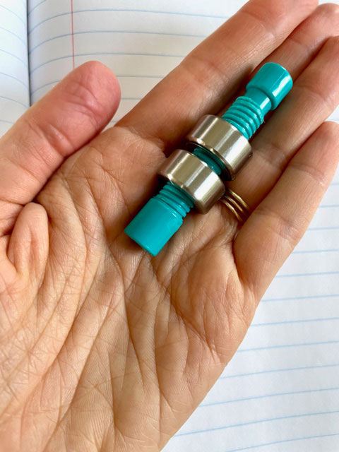 A hand holding the weighted pencil topper (just topper without a pencil) with two weights on it