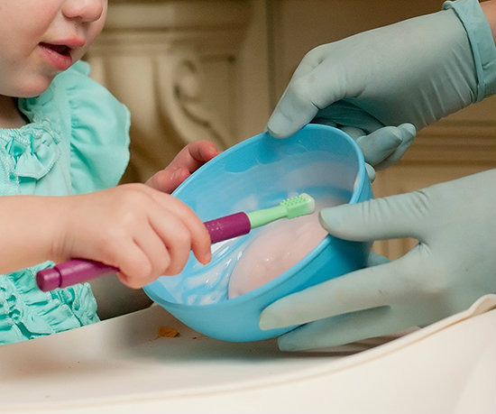 A child explores a bowl of yogurt using the Z-Vibe as a spoon with a therapist directly supervising